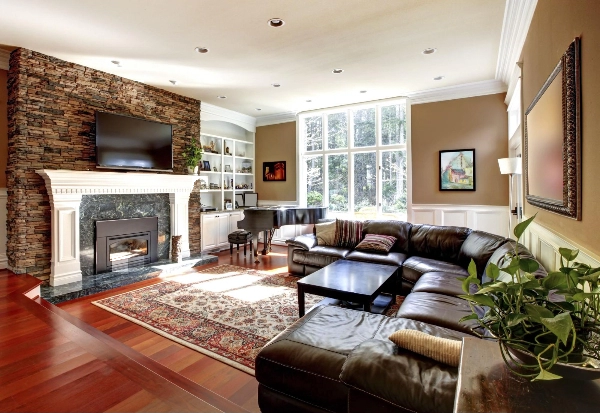 Image of wood floors in living room with fireplace, baby grand piano, and dark brown leather couch.
