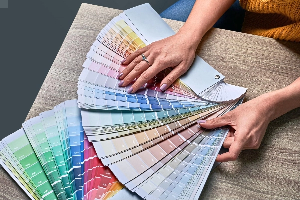 Womans hands reviewing color pallet guide over a sample of wood floors.