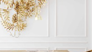 Wooden table with chairs below a white wall and a golden wall decoration.