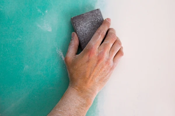 Person hand sanding drywall to prep for painting