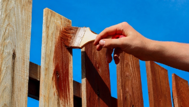 Person using a paint brush to paint a wooden fence