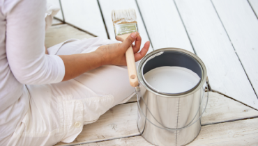 Person painting a deck with white paint.