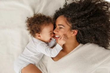 Young mother and baby laying on bed smiling