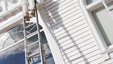 Exterior of a home being painted by a painter on a ladder