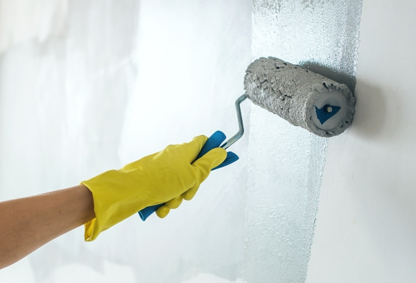 Person wearing yellow rubber glove using a paint roller to paint an interior wall