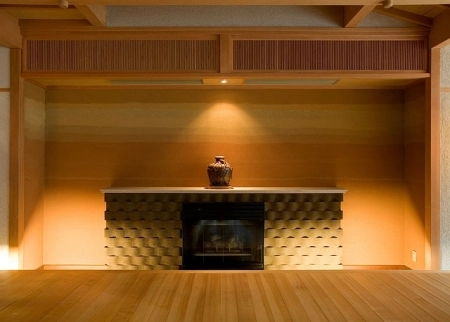 A modern fireplace with textured surround, warm lighting, and a single vase on a mantle.