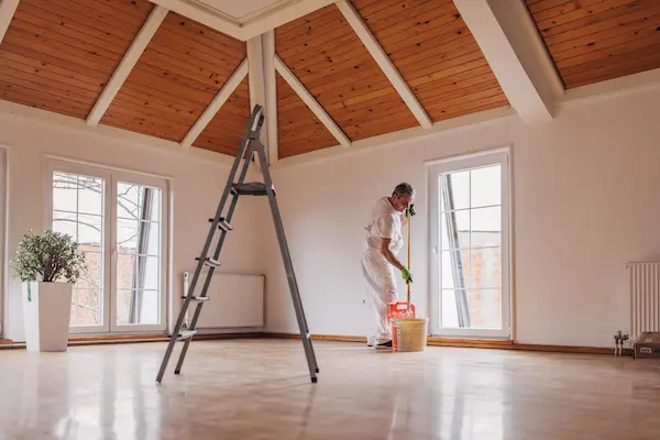 An FSP technician painting an interior room with vaulted ceilings and a ladder in the middle of the room.