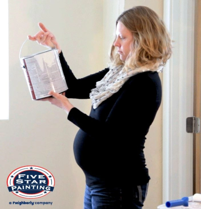 Photo of a pregnant woman staring at a paint can, Five Star Painting logo on the bottom left
