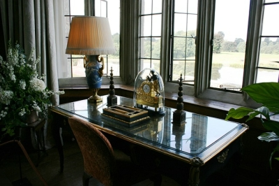 Elegant desk with lamp, clock, and books by a window overlooking a tranquil landscape.
