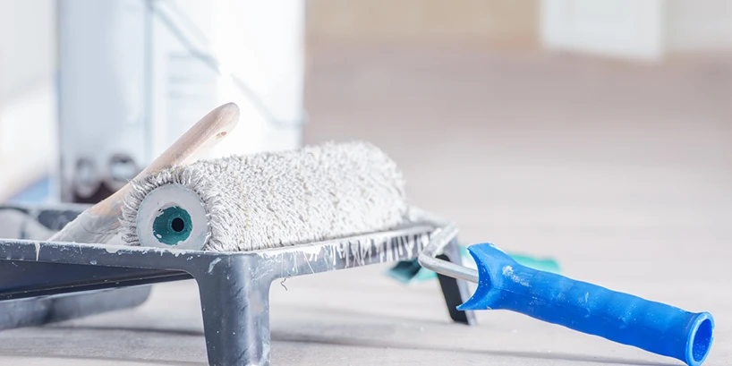 Photo of a blue-handled rolling brush wet with white paint resting on a painting tray