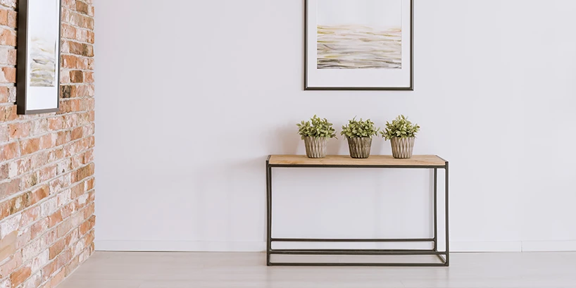 Photo of a small table with three potted plants, a brick wall, and two framed pictures