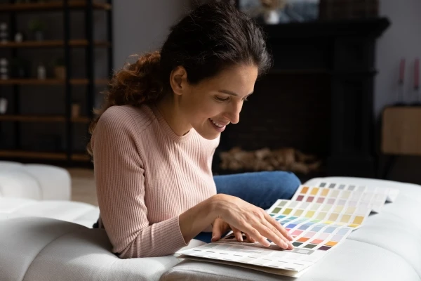 Smiling attractive, young woman resting on cozy couch, focusing on choosing colors from a swatch palette.