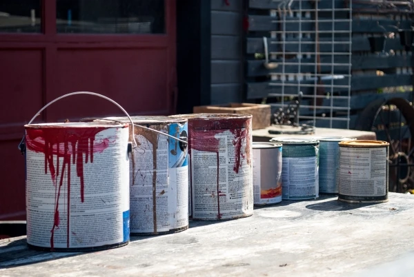 Several old paint cans in front of the garage of a residential home.