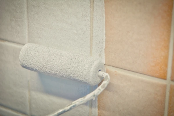 Closeup of small paint roller being used to paint over bathroom tile