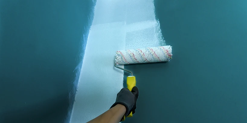 Photo of someone rolling on white paint onto a dark green wall