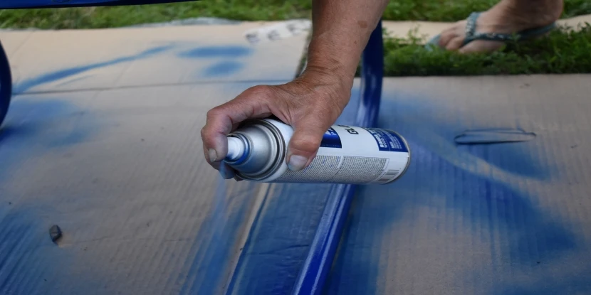 Spray painting the base of a lawn chair with blue spray paint