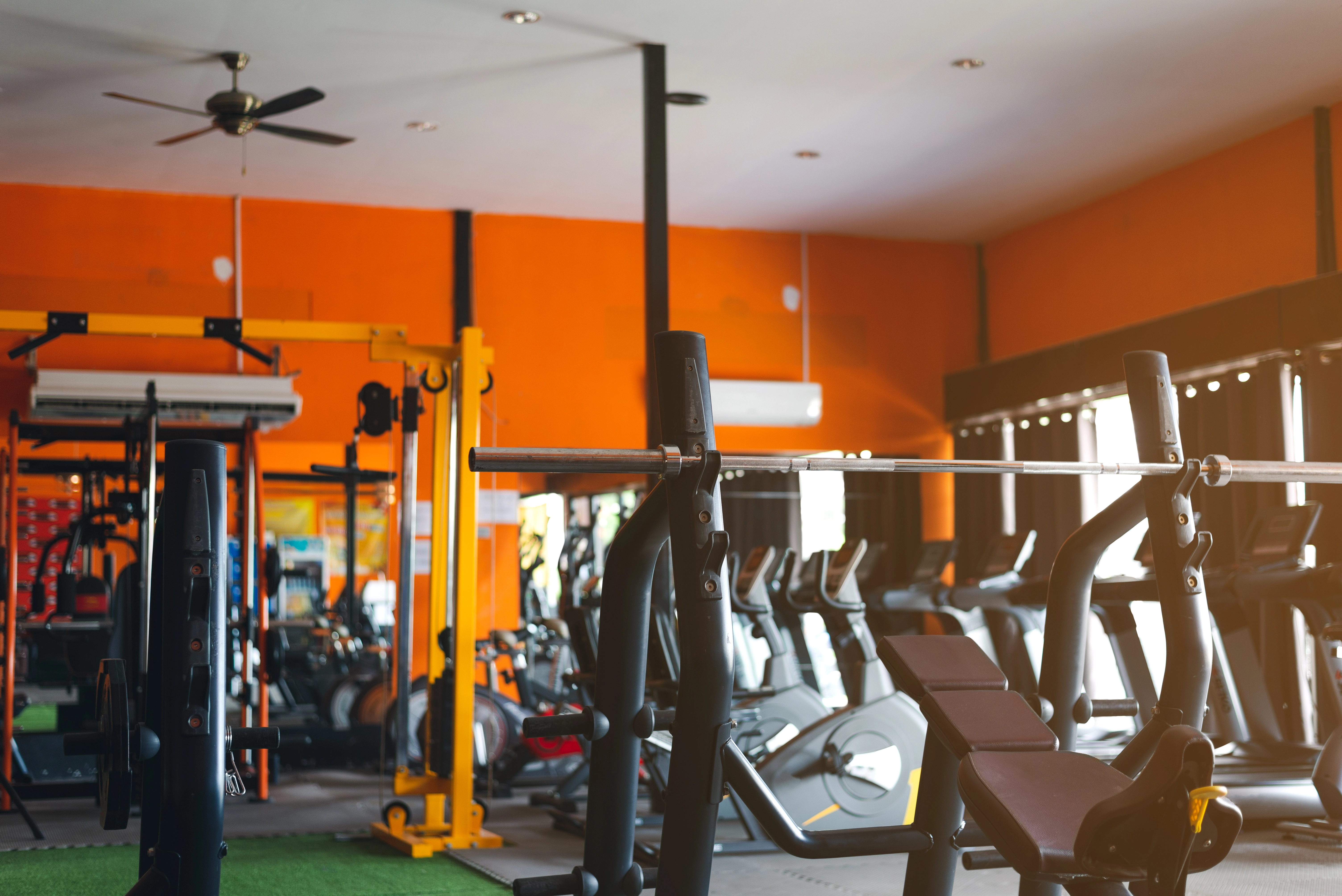 Gym with several treadmills, benches, stationary bikes, and more. Walls are painted bright orange.
