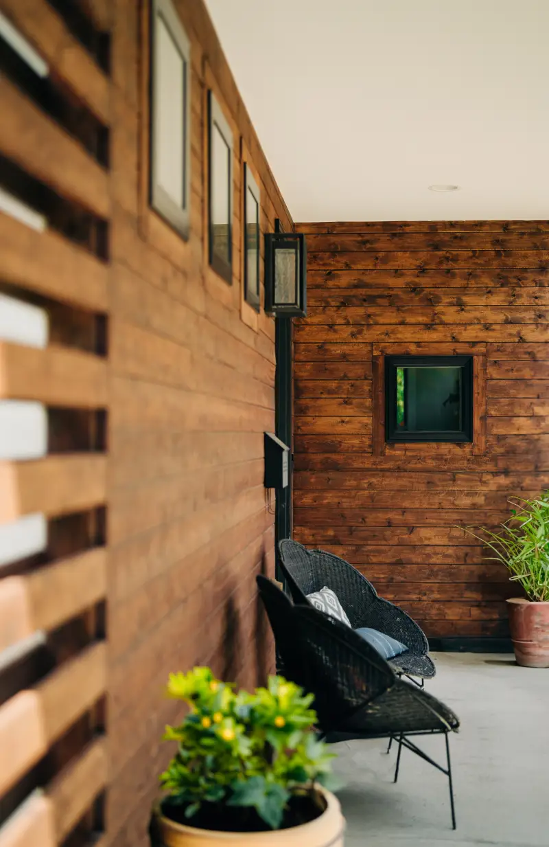 Close-up angled view of dark, stained wood siding with black window trim, accents, and cement patio.