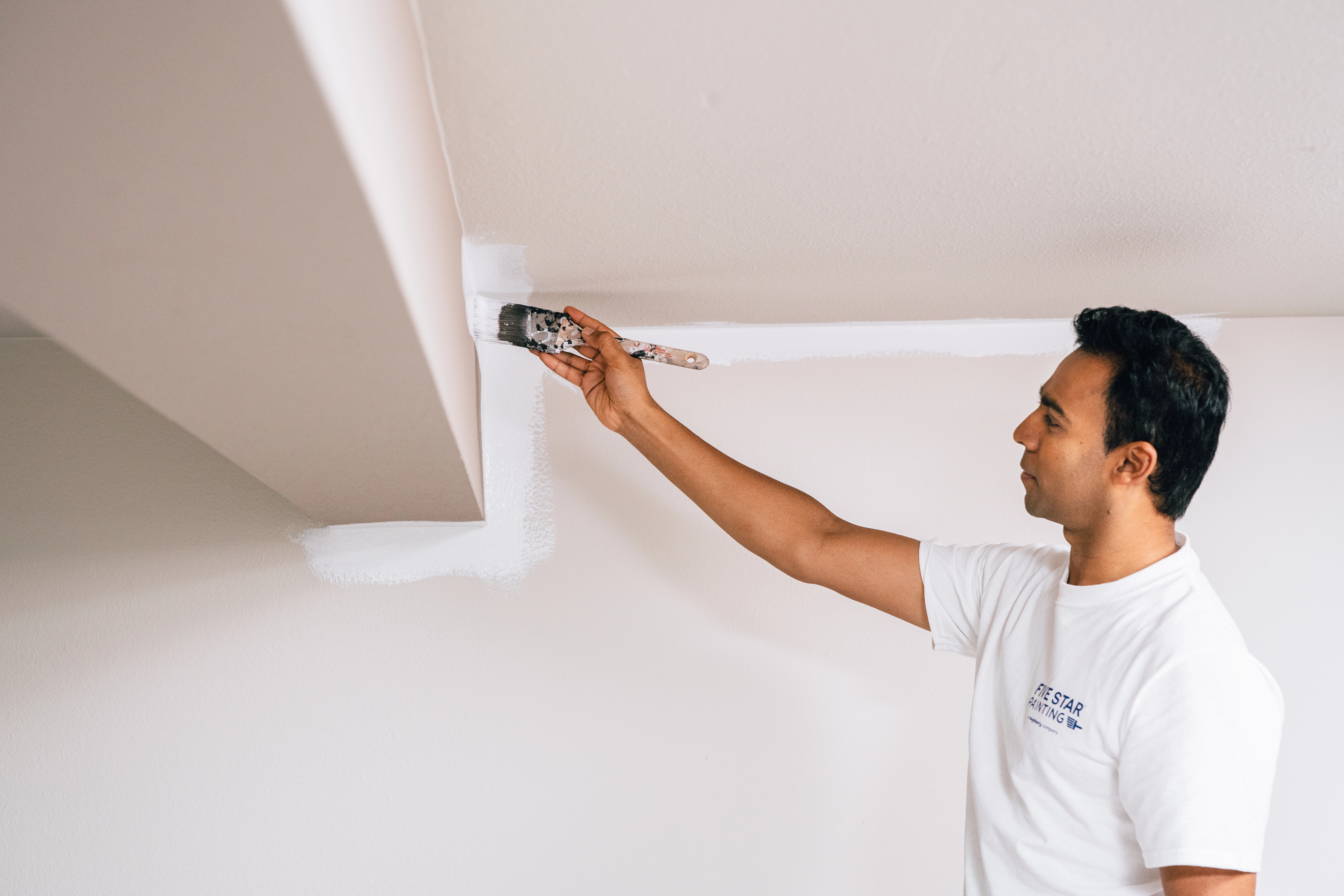 A Five Star Painting employee is painting the perimeter of a ceiling beam in a basement white. 
