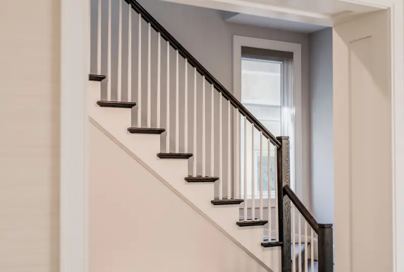 Stairway with white painted stringer, cream painted rise and walls, and wooden railing and steps.