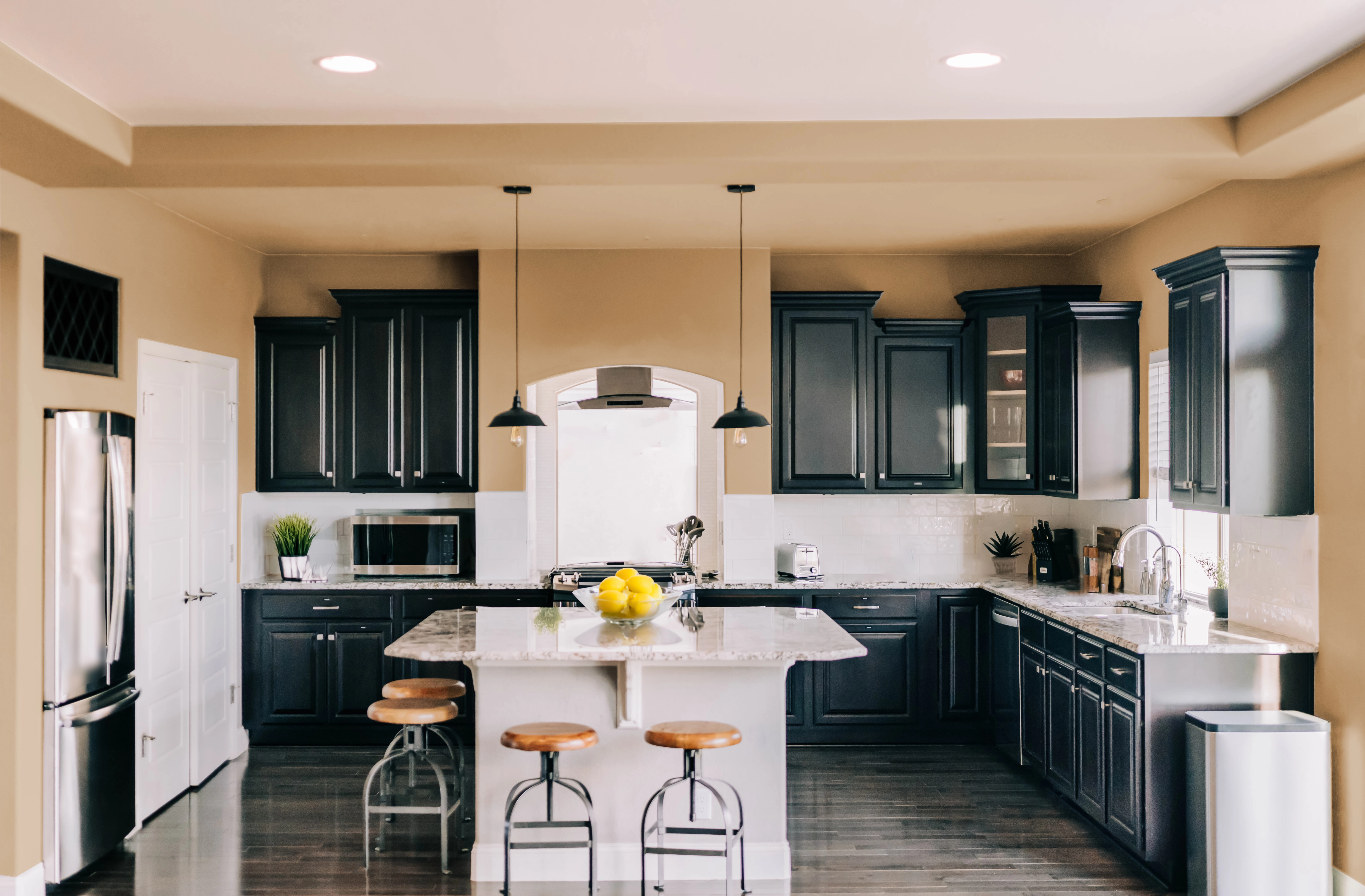 Modern kitchen with tan walls, black cabinets, white backsplash, island, doors, marble countertops.