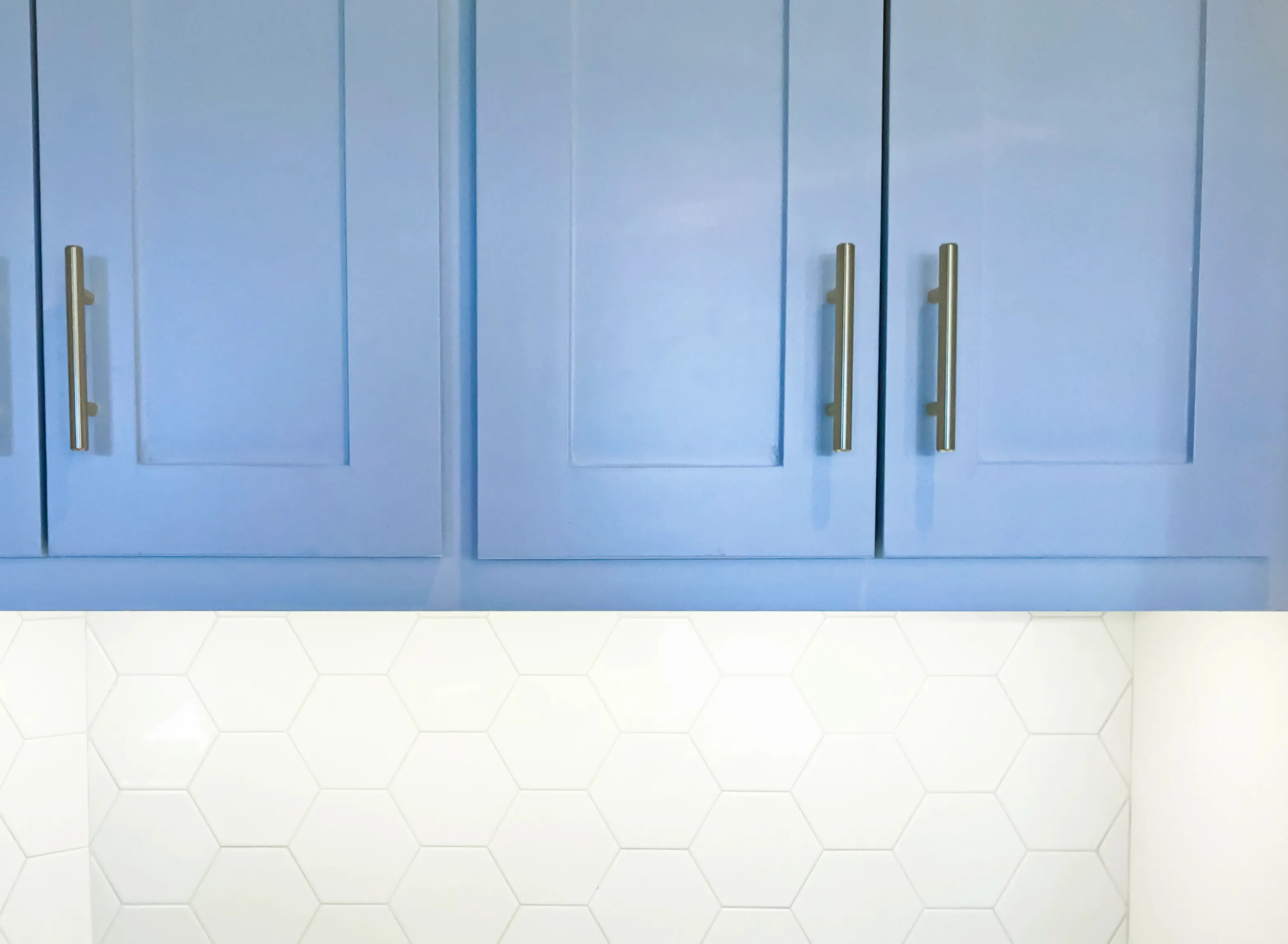 Close-up of cornflower blue painted cabinets with white hexagon tile on the wall below.