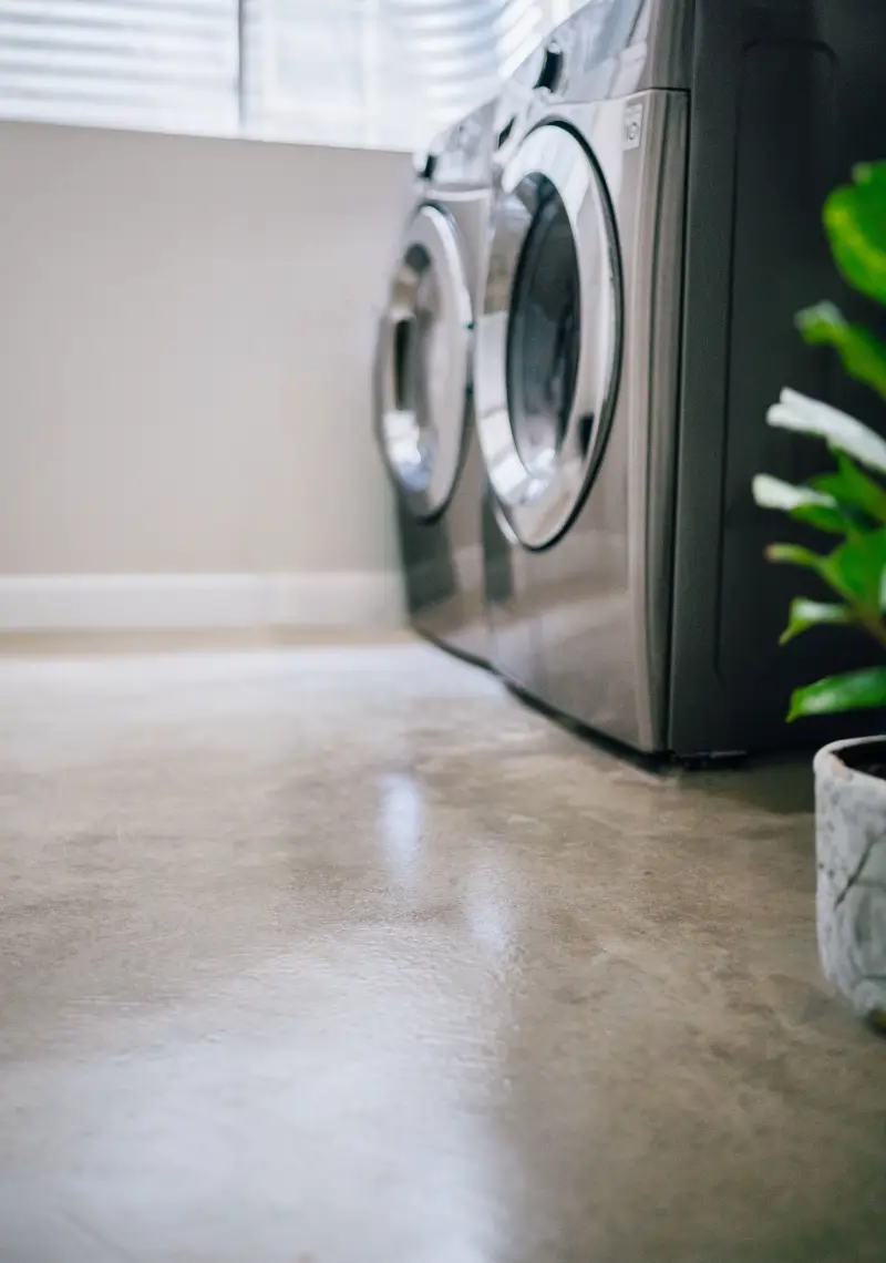 Close-up of epoxied cement floor inside interior laundry room with a washer and dryer.