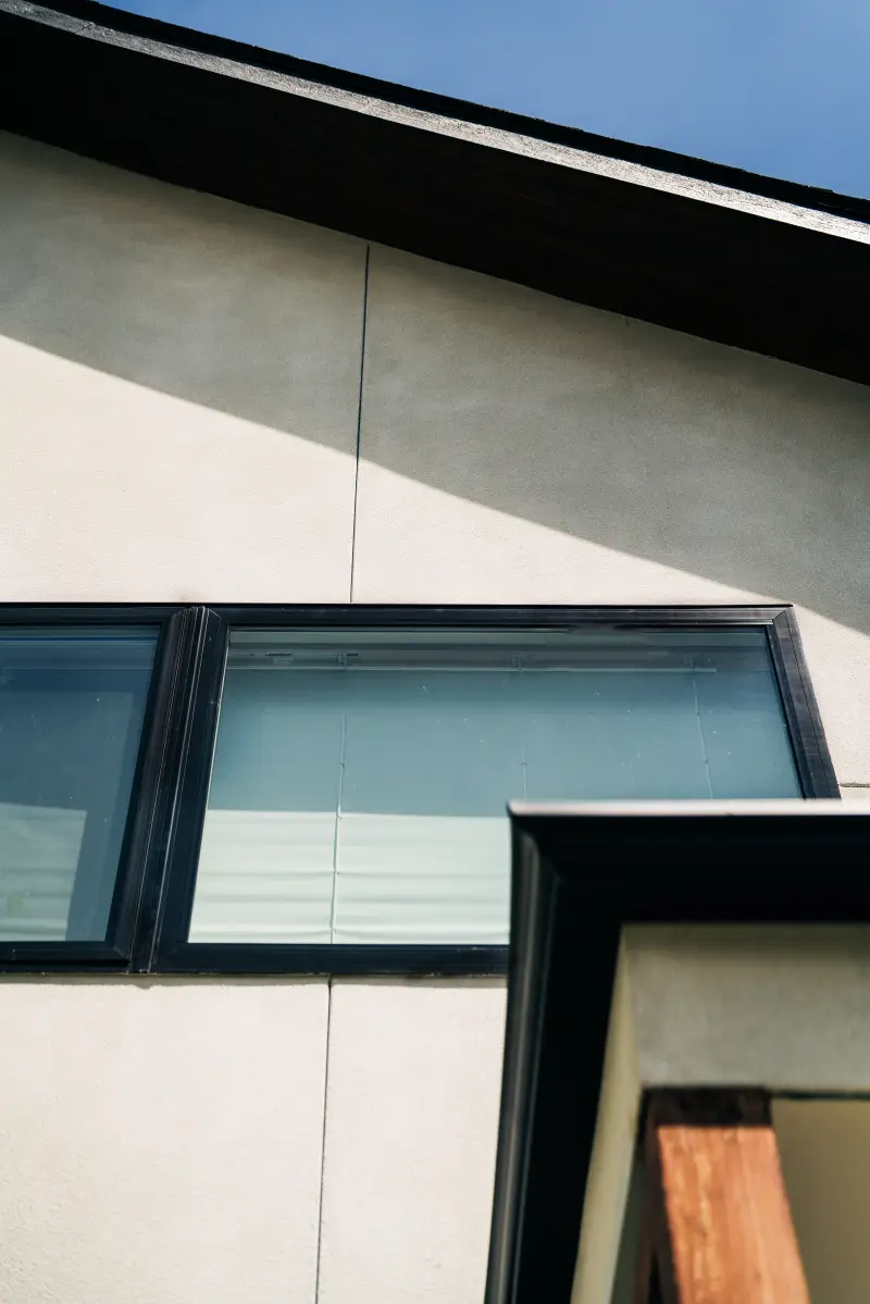 Angled shot of stucco exterior siding and roof. Windows and trim are painted black.