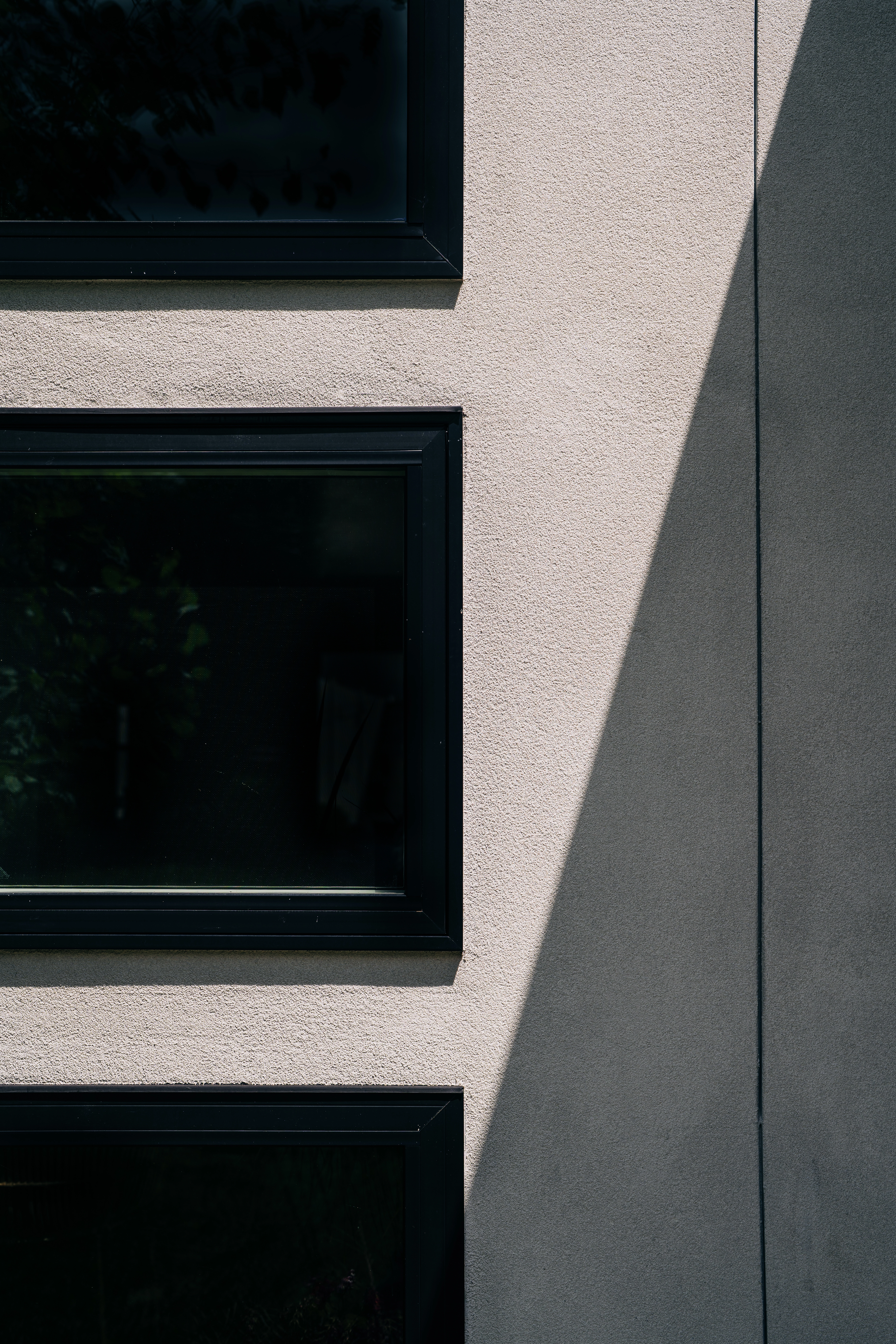 Close-up shot of stucco siding with angled shadow. Windows are tinted and trim painted black.