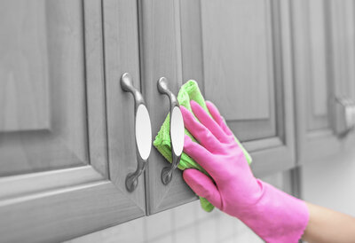 Person wearing pink glove and using green cloth to clean a cabinet door