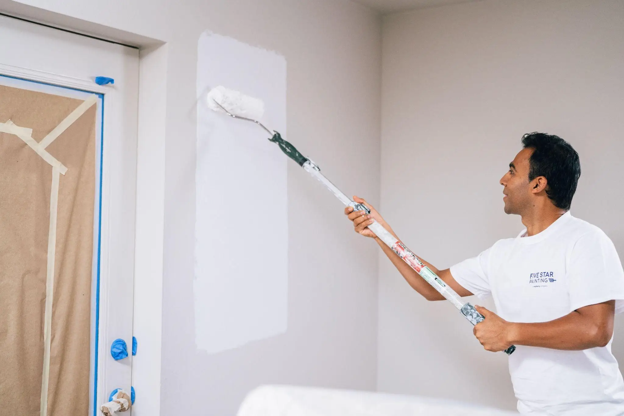 Five Star Painting profession using a roller brush to paint walls with white primer.