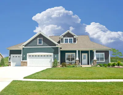 Two story house in green with a white garage and big blue sky with clouds in background