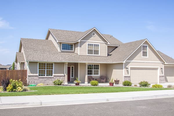 Two story tan house with manicured lawn and garage.