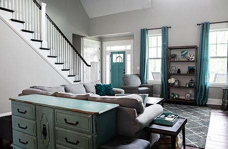 A living room with teal accents featuring furniture, bookcases, and a staircase on the left.