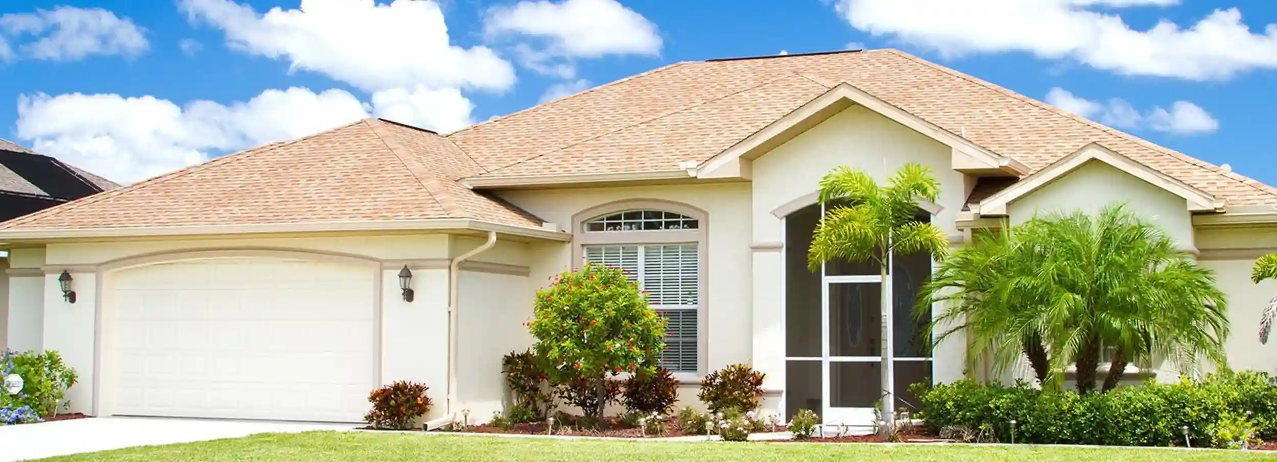 A single story tan home with landscaped front lawn and Floridian plants.