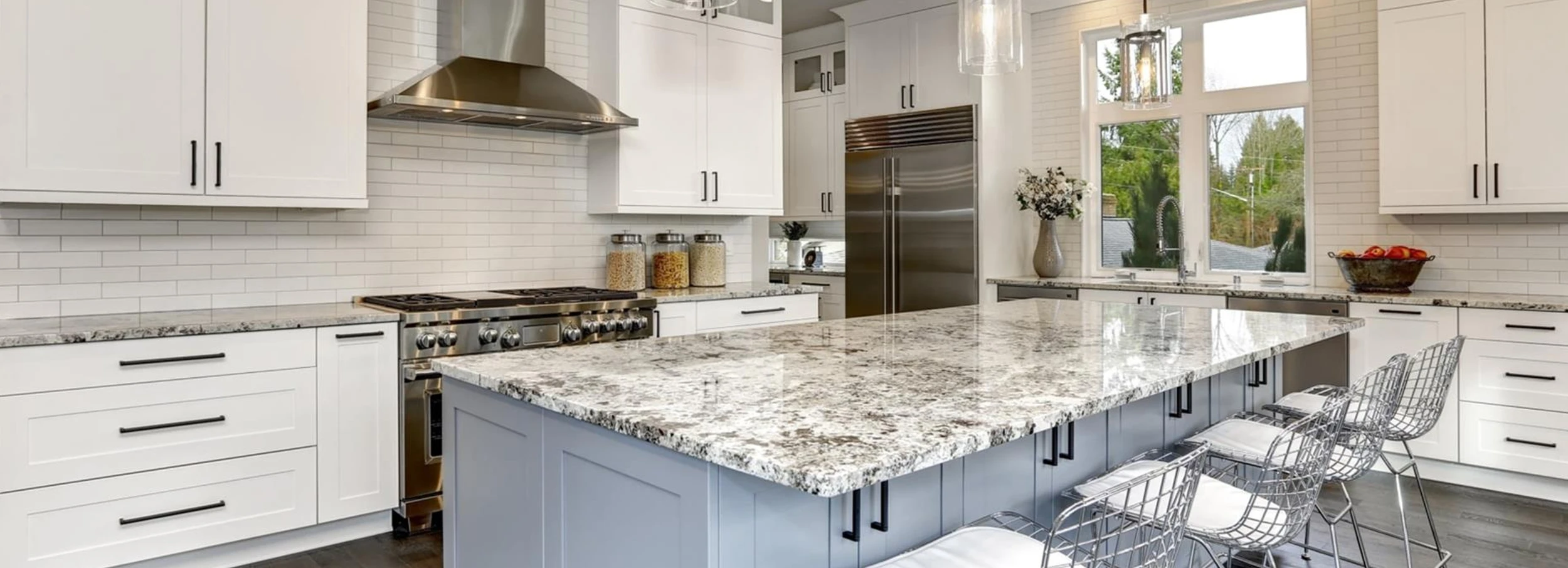 Marble top kitchen island in large, bright modern kitchen with white cabinets and dark hardwood floor.