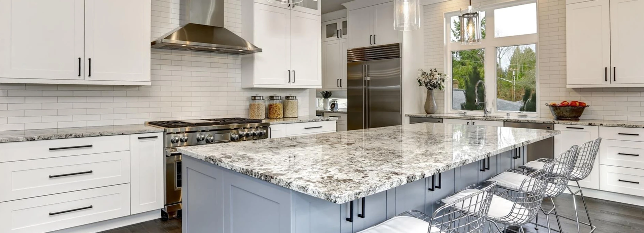 Modern kitchen with granite countertops, a grey island and white cabinets with stainless steel appliances.