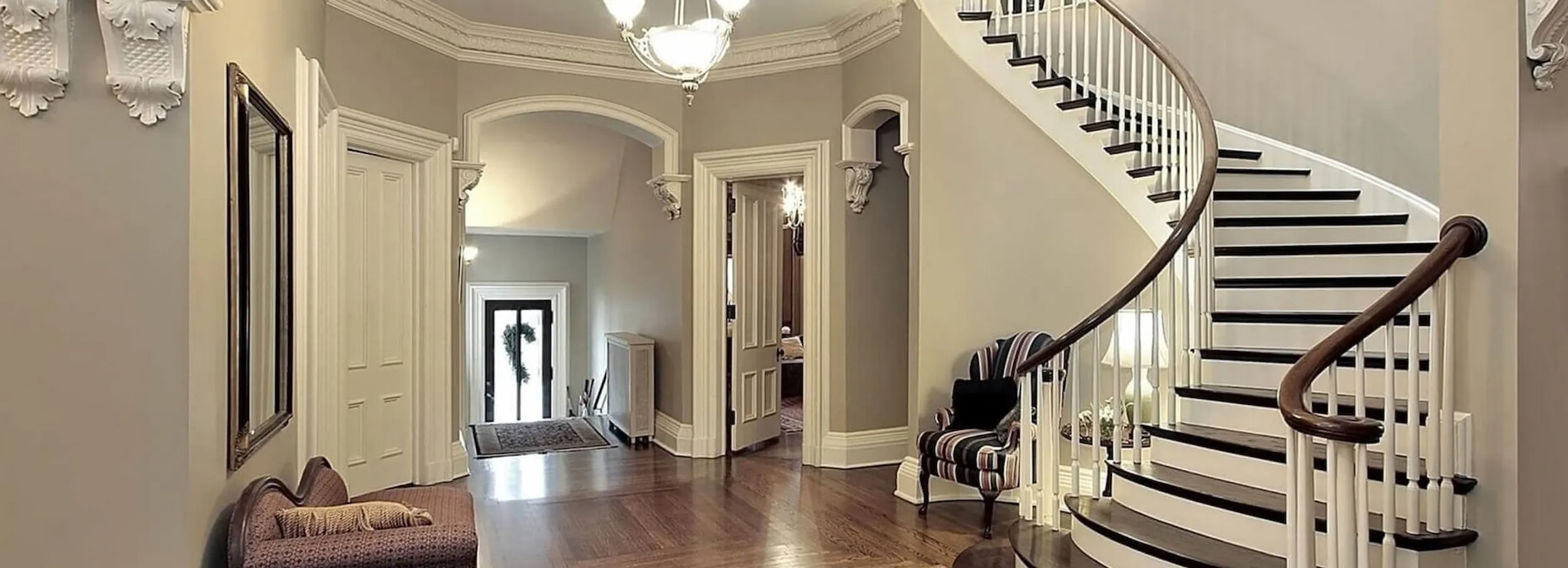 The entryway of a home with a curving staircase to the right and seating throughout the foyer.