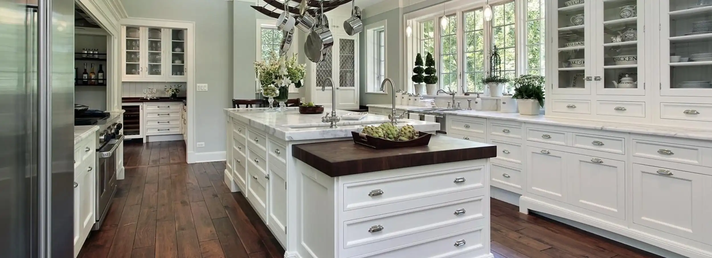 Marble top kitchen island in large, bright modern kitchen with white cabinets and dark hardwood floor.