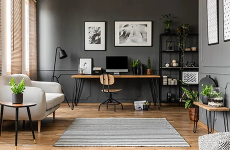 Interior of a living room with wood flooring, gray paneled walls, a couch, desk and shelves.