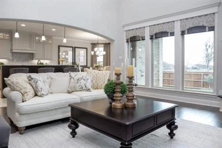 Living room with white walls, tall windows and a couch and coffee table with the kitchen in the background.