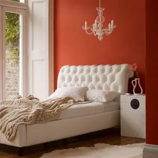 White bed with headboard beside French patio doors inside bright bedroom painted orange.