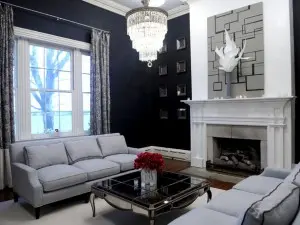 Living room with dark blue walls decorated with pair of gray sofas, chandelier and fireplace.