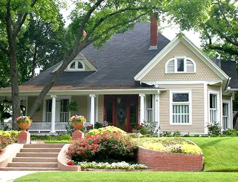 A brown cottage with nice lawn and stairs leading to sidewalk.