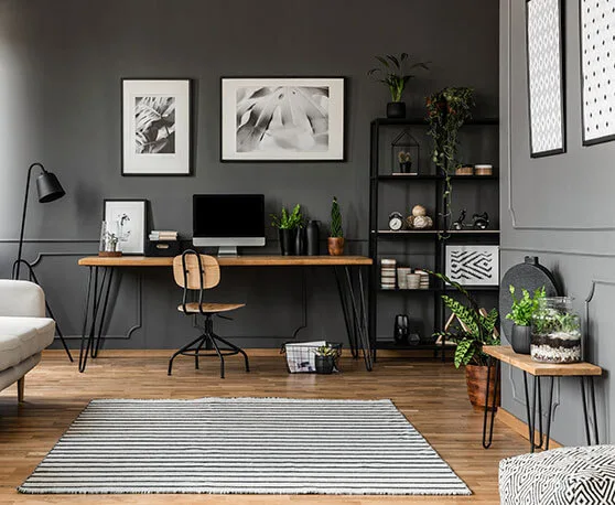 Interior of a living room with wood flooring, grey painted walls, a couch, desk and shelves.