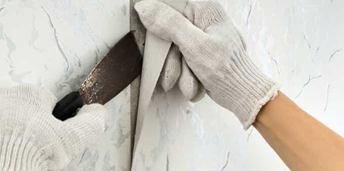 a gloved hand repairing wallpaper with a putty knife