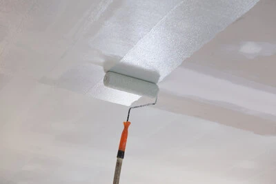 Paint roller applying white paint on a ceiling