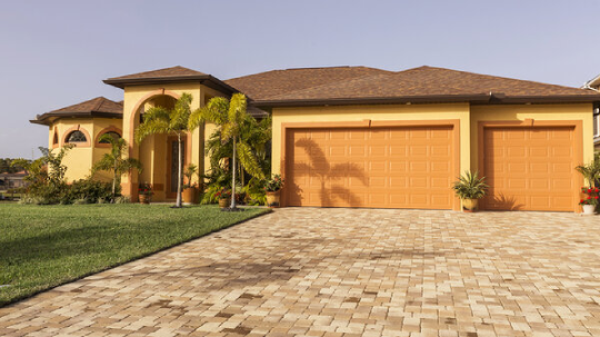 Exterior of a mediterranean house painted in beige with a three car garage and palm trees in front.