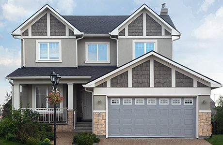 Exterior of a grey painted house with white siding and a large garage with a dark grey painted door.