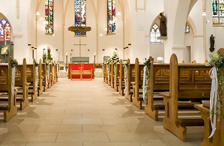 The interior of a church with stained glass windows, white walls and an aisle leading to the stage with benches on both sides of the aisle. 